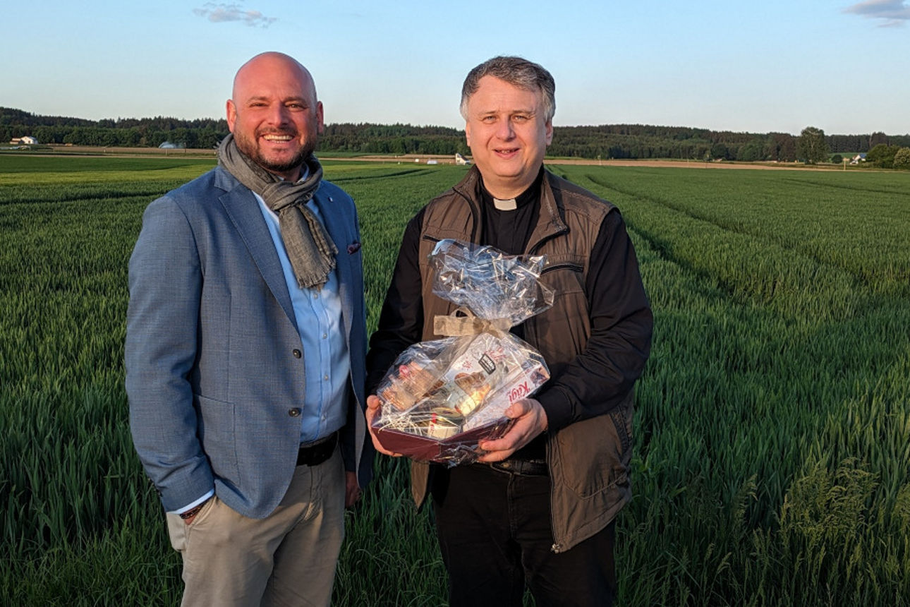 Vorstand steht mit dem Dekan mit Geschenkkorb vor einem grünen Feld
