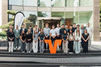 Mitarbeitende der VR Bank RheinAhrEifel eG vor modernem Bankgebäude, gruppiert um großes oranges V-Logo