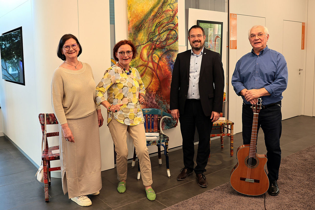 Vier Personen bei Kunstausstellungseröffnung vor abstraktem Gemälde und bemalten Stühlen in Daun