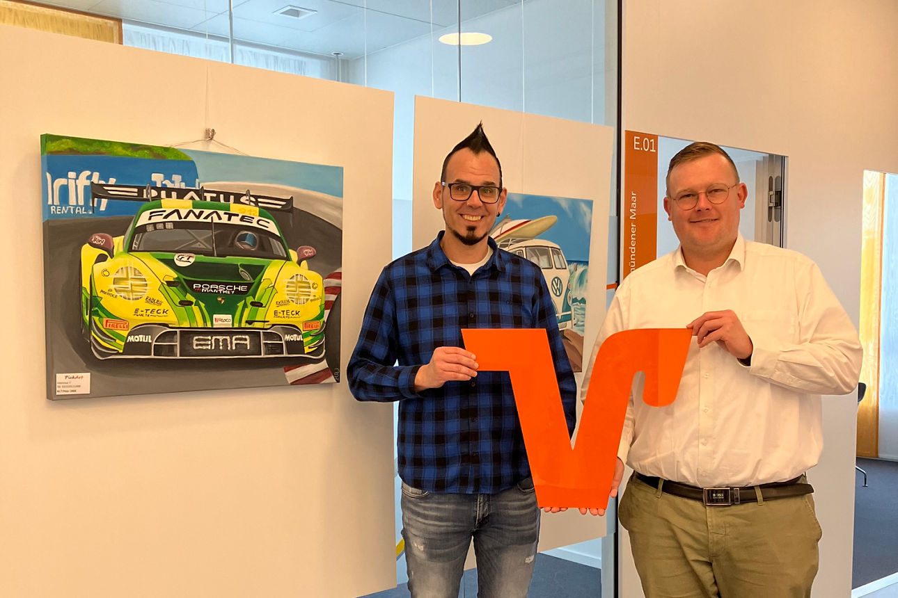 Zwei Männer mit VR-Logo vor Fahrzeug-Gemälden des Künstlers PoArt in der Filiale Daun