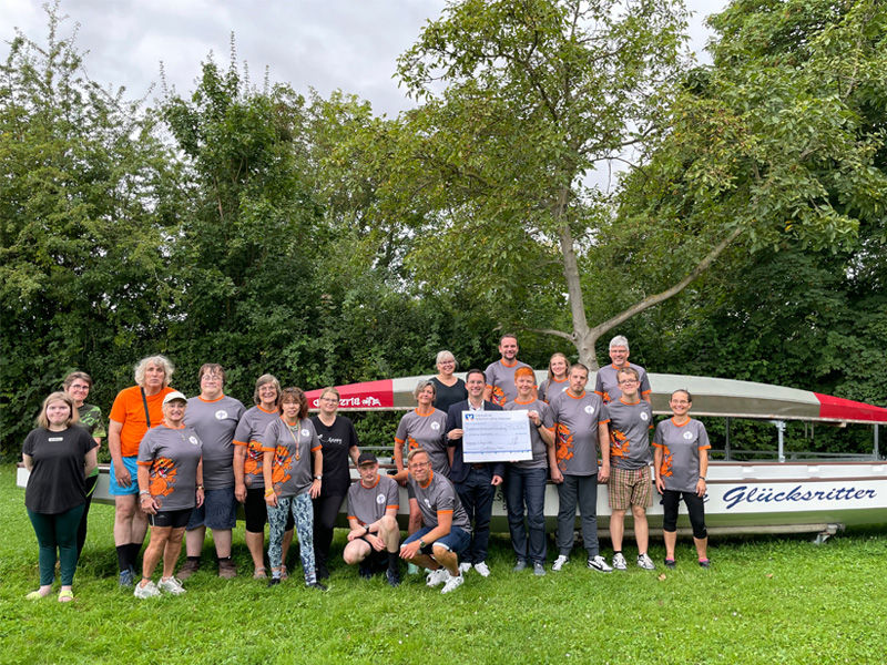 Die Glücksritter bei der Spendenübergabe mit dem Geschäftsstellenleiter aus Hildesheim, Timo Hauptmann, vor dem Drachenboot.