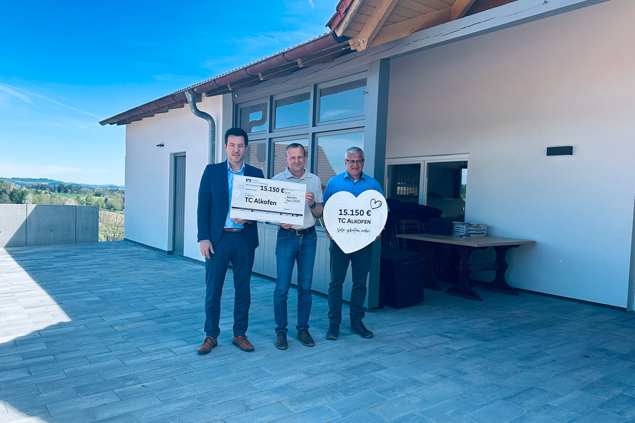 Drei Personen mit Scheck vor einem Haus