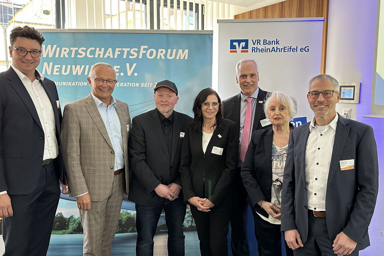 Mehrere Personen stehen in einem Raum vor diversen Roll-Ups zu einem Gruppenbild zusammen.