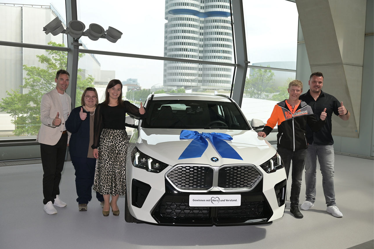 Kunde der VR-Bank mit Mitarbeitern und dem neuen BMW in der Austellungshalle