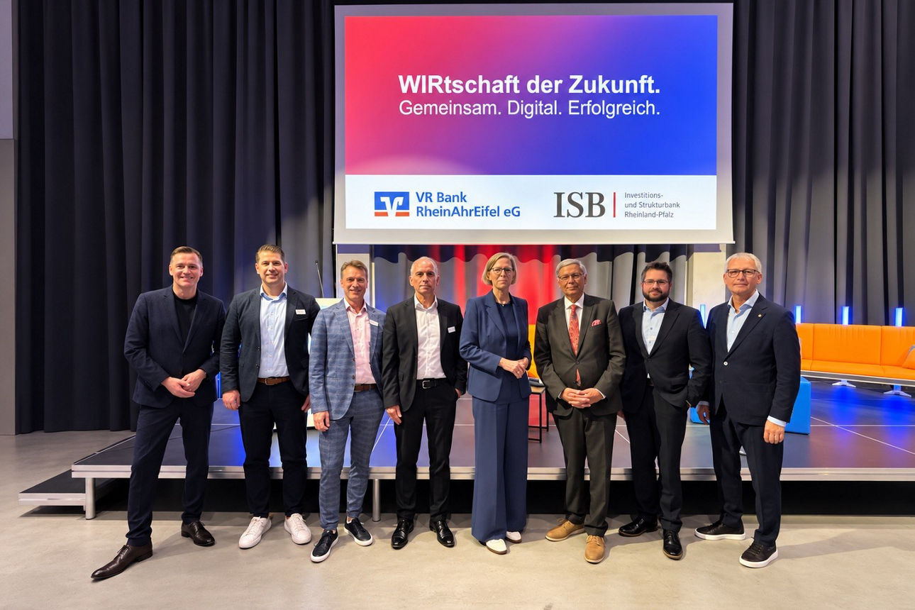 Gruppenfoto von acht Personen vor der Leinwand „WIRtschaft der Zukunft“ der VR Bank RheinAhrEifel eG