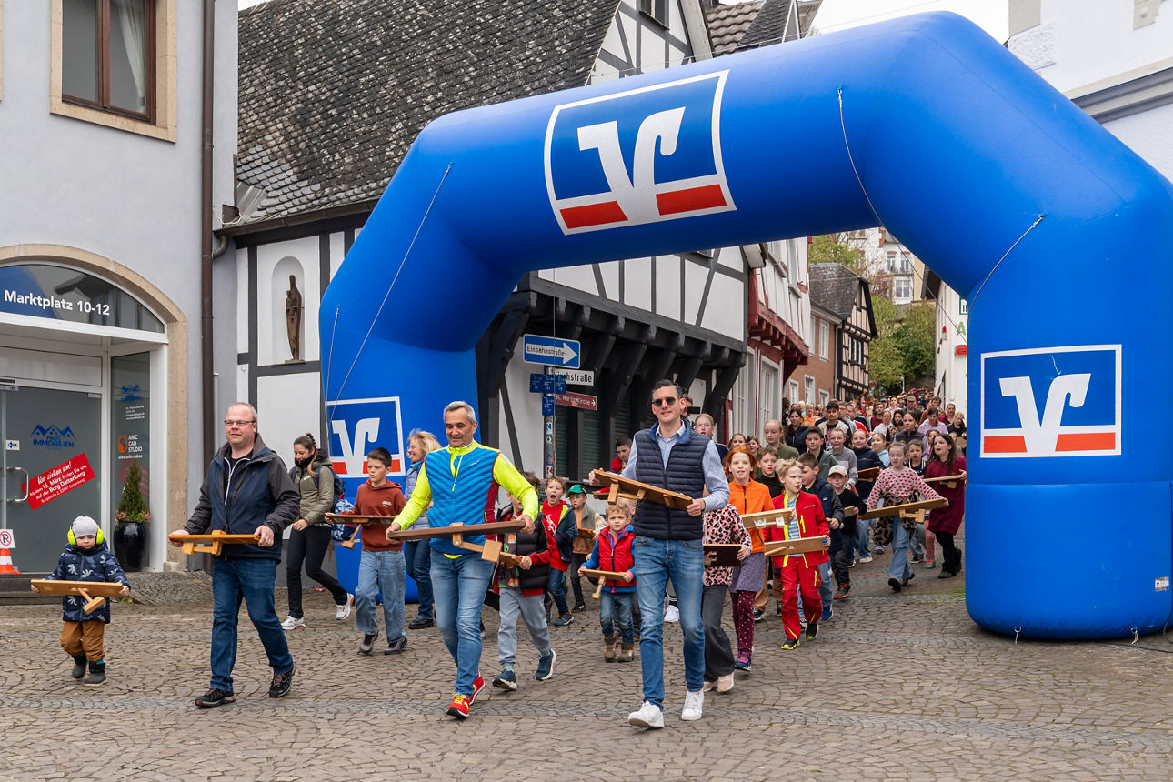 Kinder und Erwachsene mit Klappern ziehen durch die Linzer Altstadt, im Hintergrund ein VR-Bank-Torbogen