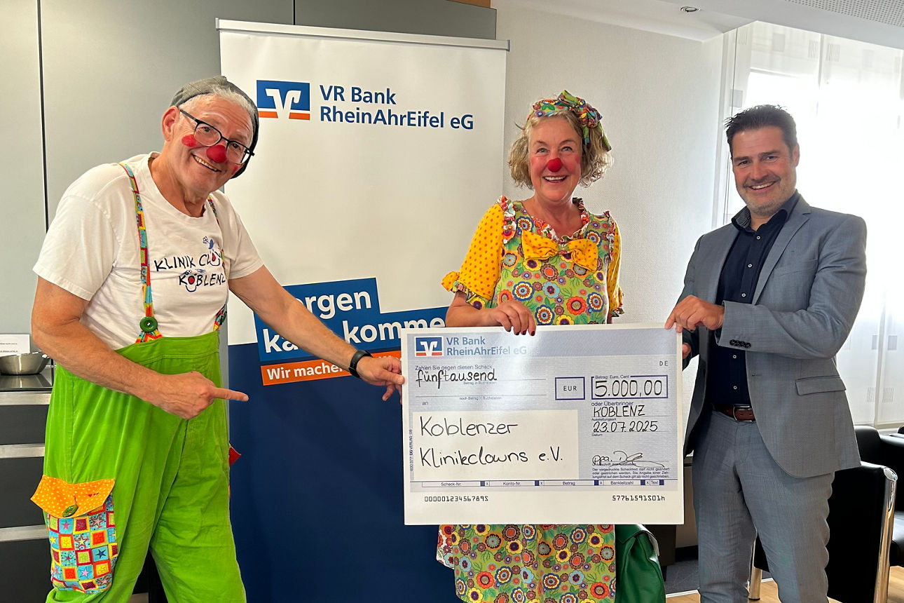 Auf dem Bild sind drei Personen zu sehen. Zwei davon sind als Clowns verkleidet, die dritte Person trägt einen Anzug. 