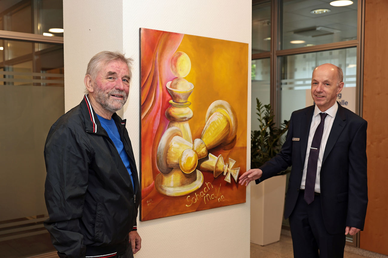 Künstler und Bankvertreter präsentieren Gemälde „Schach Matt" mit Schachfiguren bei Ausstellung in Adenau