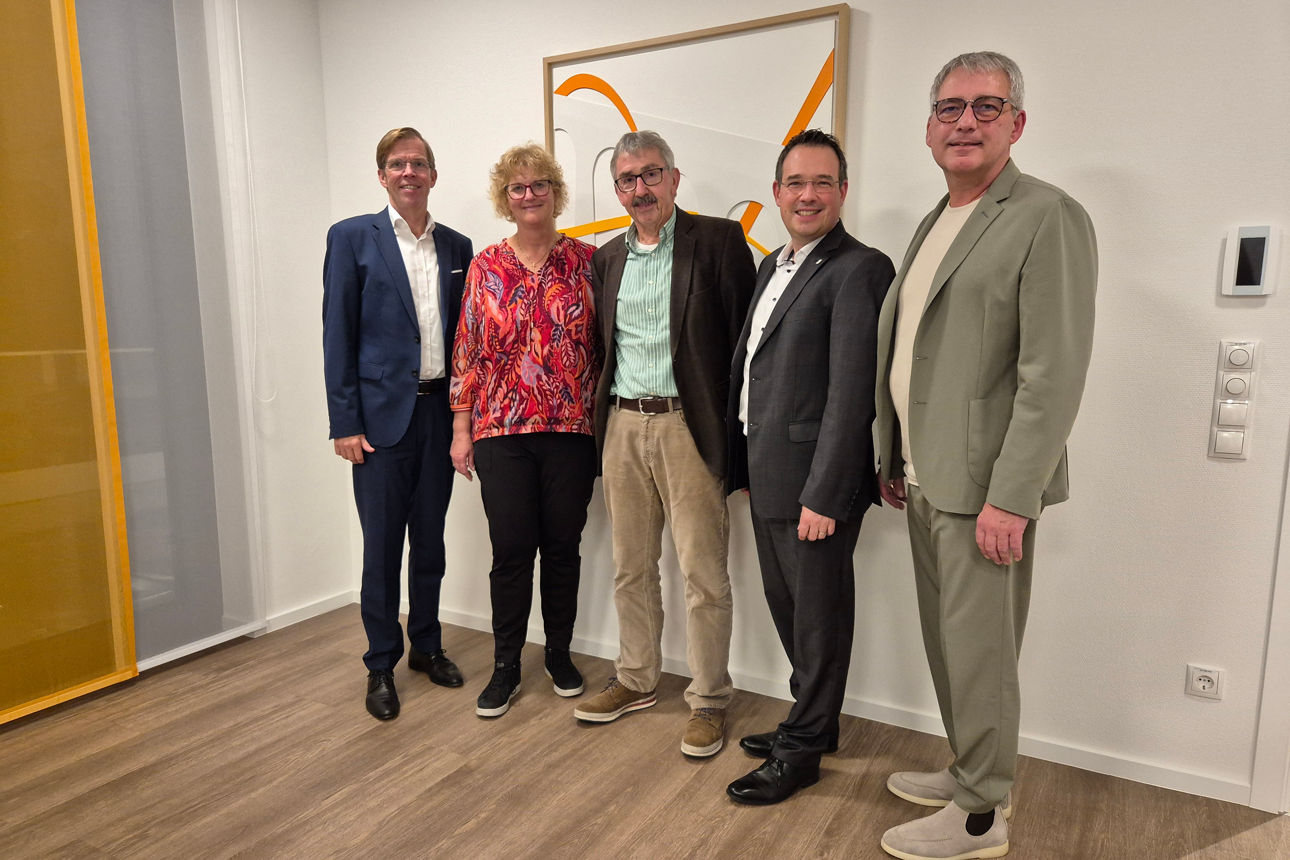Fünf Personen stehen in einem Raum zu einem Gruppenbild zusammen.