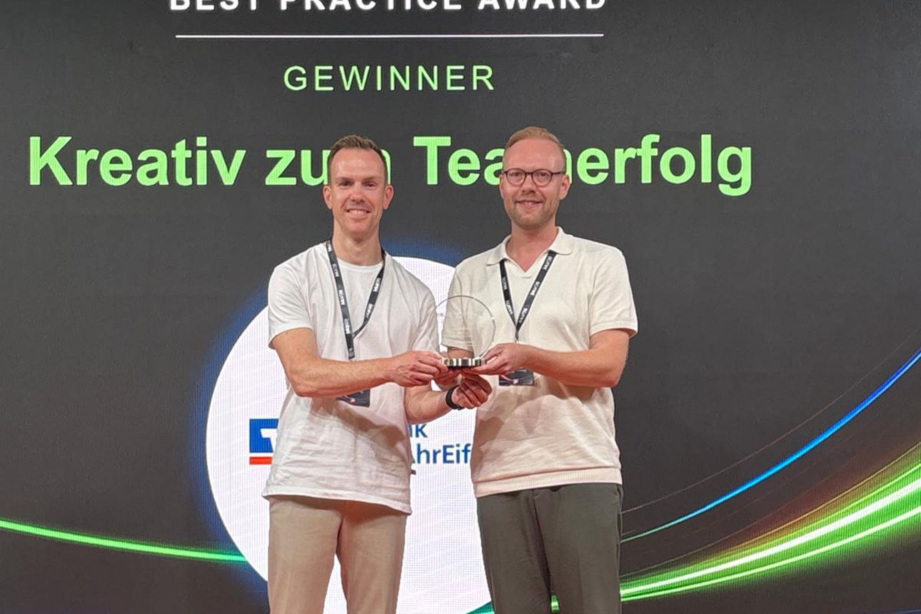 Zwei Männer präsentieren MuV26 Forward Best Practice Award; im Hintergrund: Gewinner „Kreativ zu Teamerfolg“