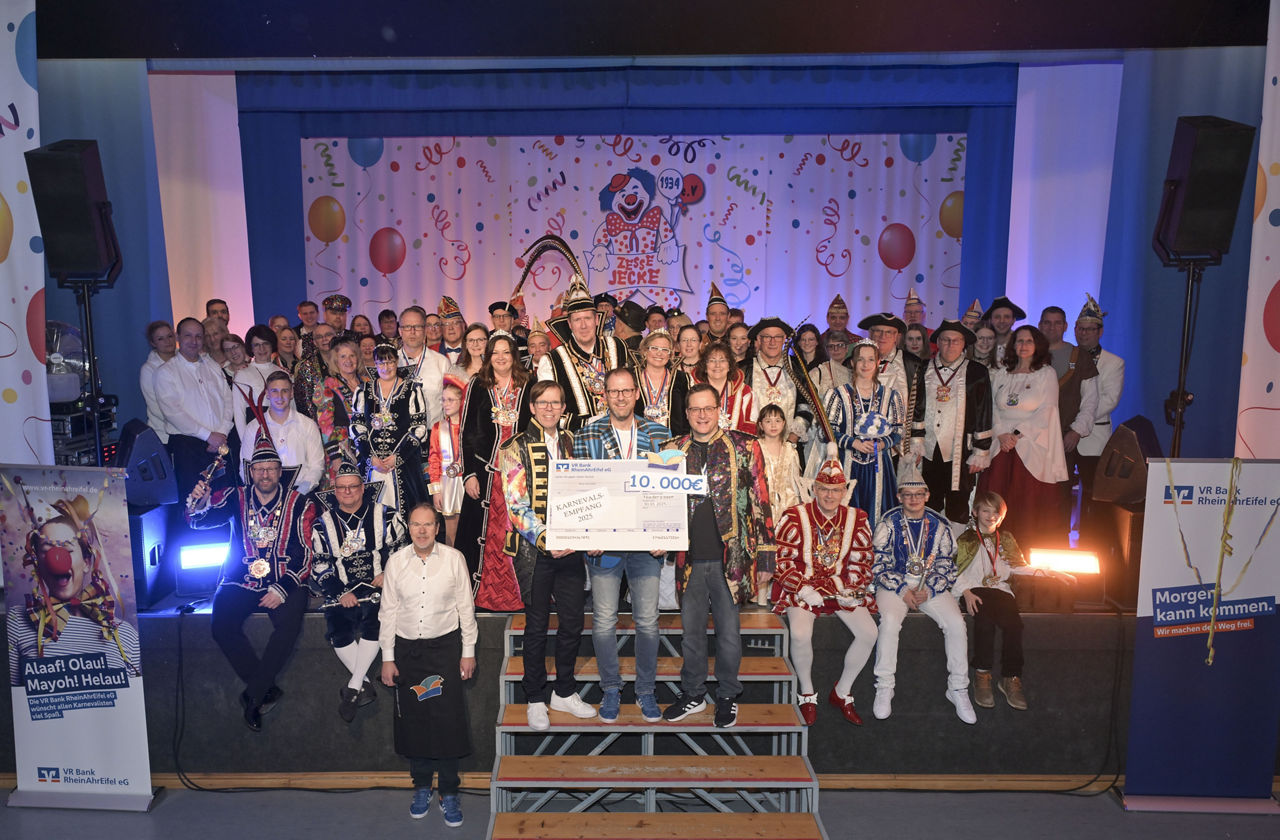 Mehrere Personen in karnevalistischer Kleidung sitzen und stehen zu einem Gruppenbild zusammen.