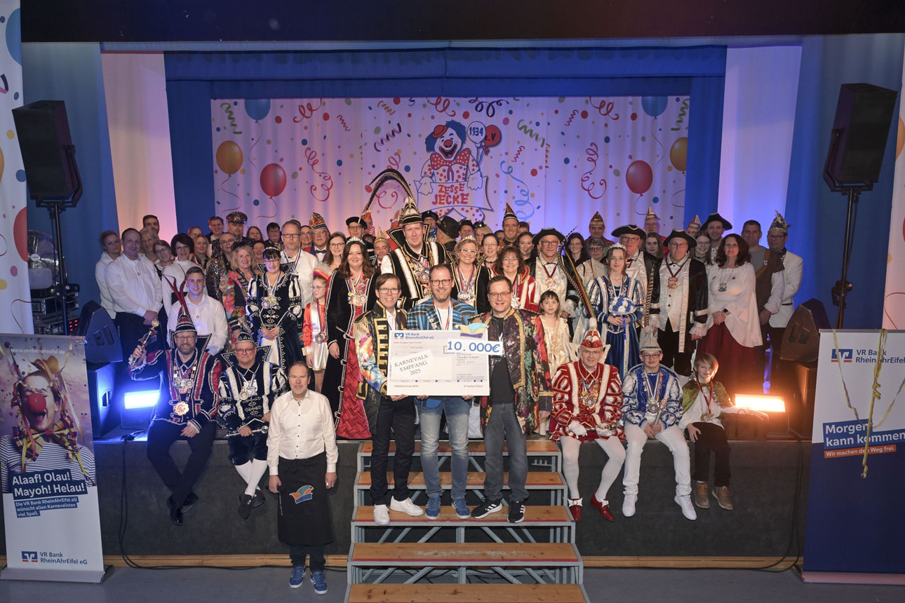 Mehrere Personen in karnevalistischer Kleidung sitzen und stehen zu einem Gruppenbild zusammen.