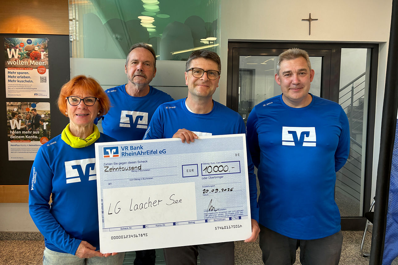 Vier Personen in blauen Shirts halten einen großen Spendenscheck über 10.000 € in die Kamera