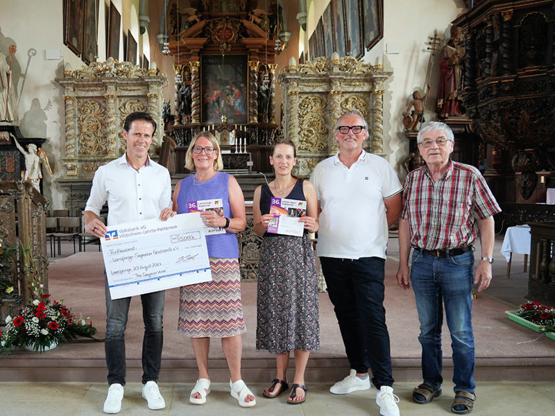 Drei Männer und zwei Frauen stehen in einer Kirche und halten einen Überreichungsscheck in der Hand.