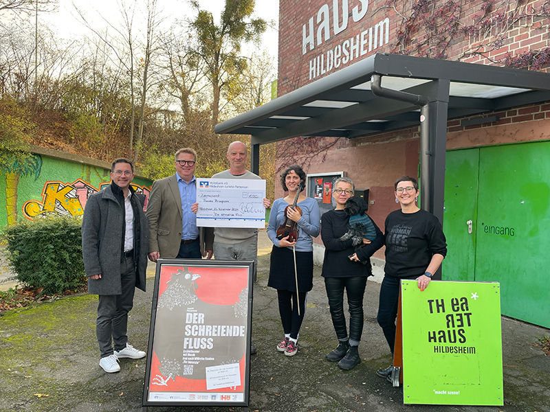 Drei Männer und drei Frauen stehen vor dem Theaterhaus Hildesheim und halten einen Überreichungsscheck in der Hand.