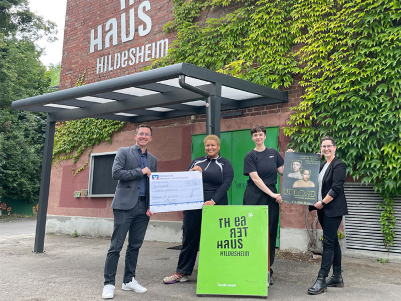 Ein Mann und drei Frauen halten einen Überreichungsscheck vor dem Theaterhaus Hildesheim hoch.