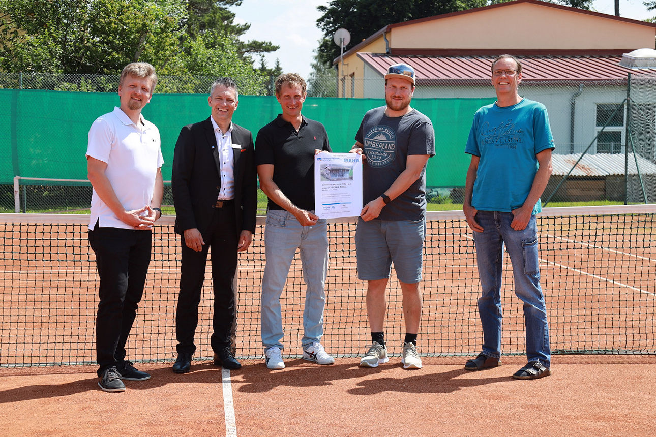 Mitglieder des Tennisclubs stehen mit einer Urkunde nebeneinander mit einem Mitarbeiter auf dem Tennisplatz