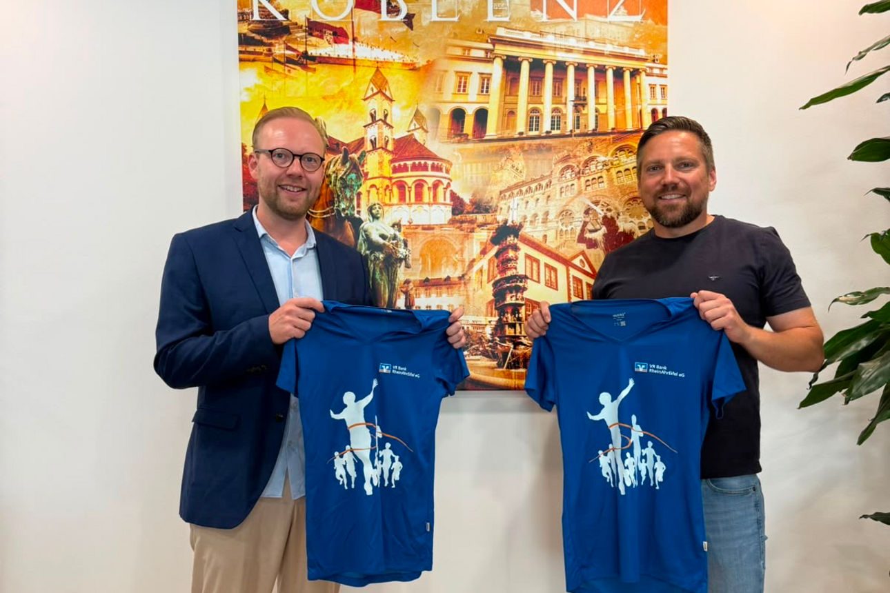  Zwei Männer präsentieren blaue Marathon-T-Shirts vor einem Poster mit der Aufschrift „KOBLENZ“.