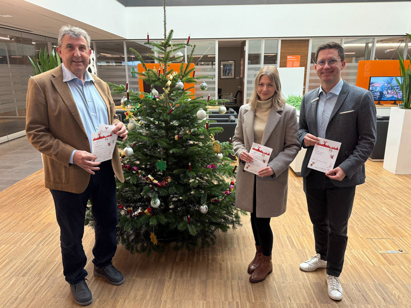Zwei Männer und einer Frau stehen vor einem Weihnachtsbaum und halten jeweils einen Wunschzettel in der Hand