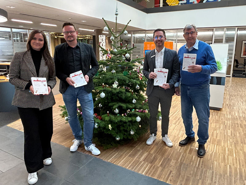 Eine Frau und drei Männer stehen vor dem Weihnachtsbaum in der Hauptstelle Hildesheim und halten die Wunschzettel in der Hand