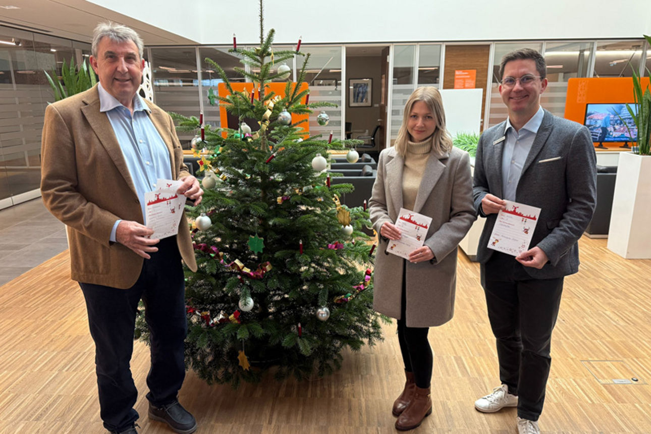 Zwei Männer und eine Frau stehen vor einem Weihnachtsbaum und halten jeweils einen Wunschzettel in der Hand