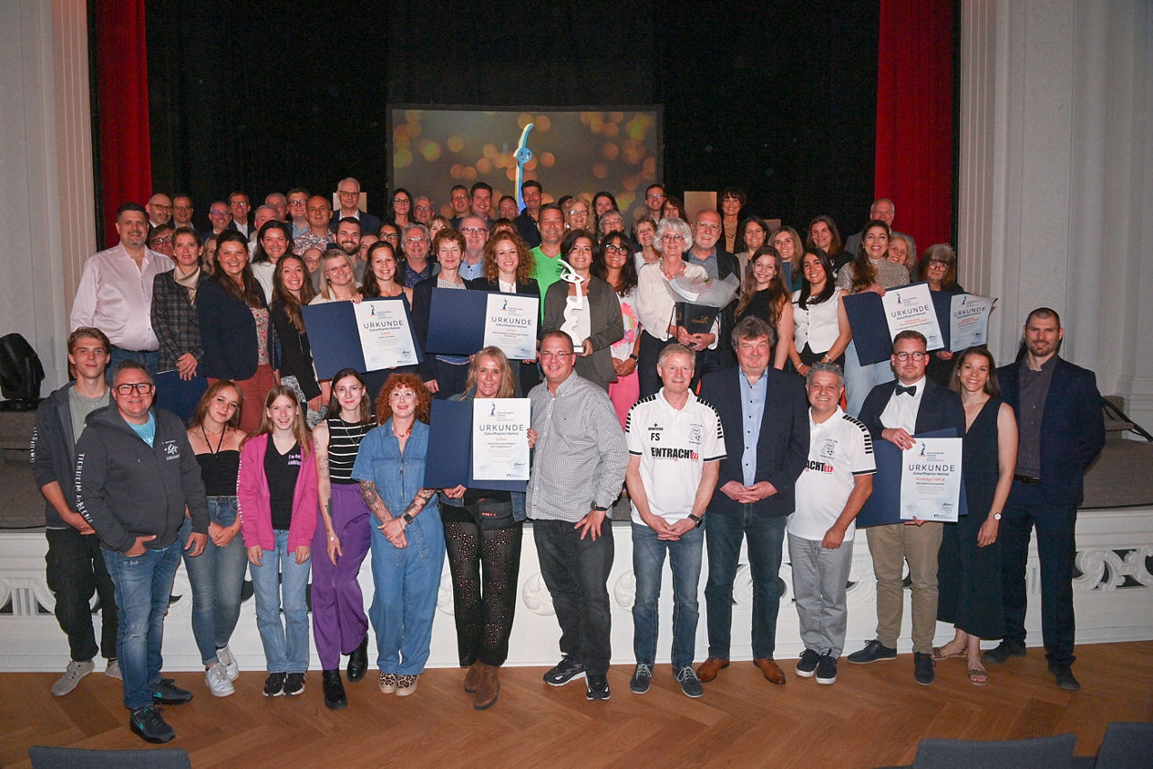 Das Bild zeigt viele Personen, die sich auf und vor einer Bühne zu einem Gruppenbild aufgestellt haben.