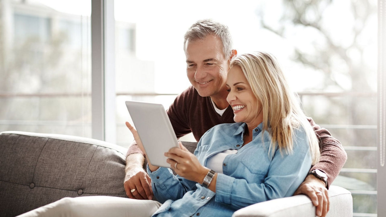 Ein älteres Paar sitzt auf der Couch und schaut gemeinsam in ein Tablet