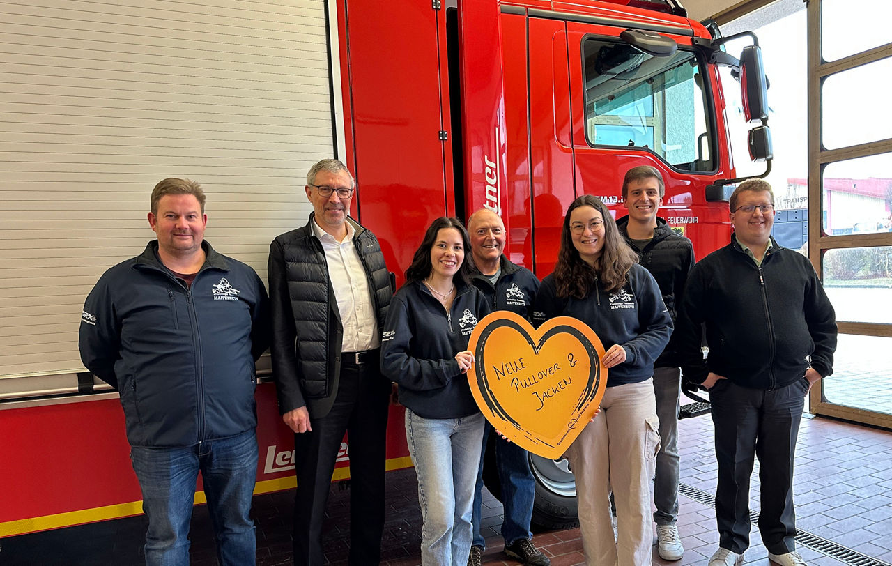 Eine Gruppe von Menschen posiert gemeinsam vor einem Feuerwehrauto