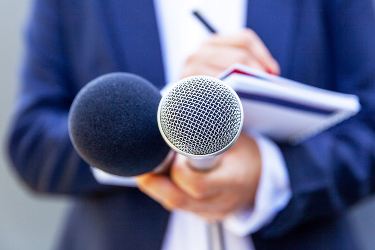 Frau mit zwei Mikrofonen und einem Notizblock in der Hand