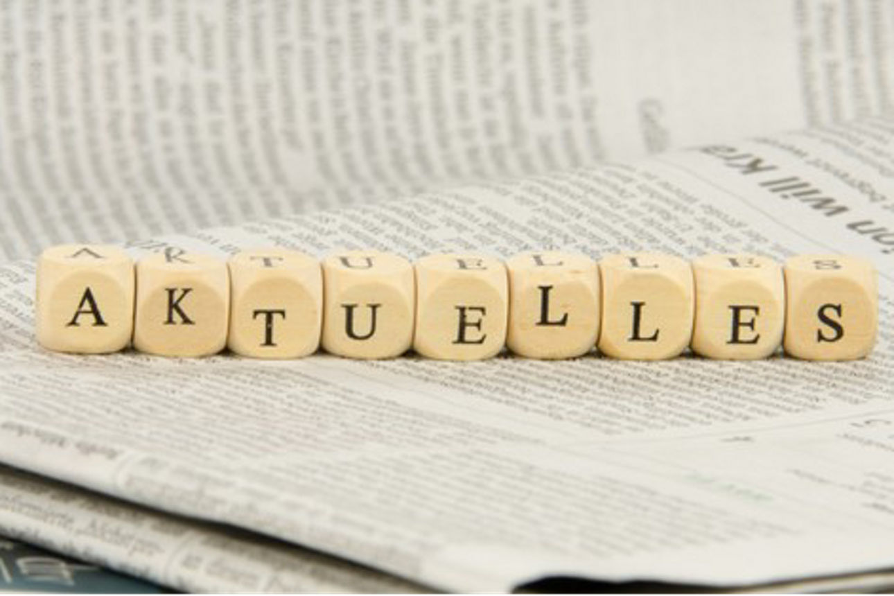 Würfel mit Buchstaben liegen auf einer Zeitung und sind als das Wort "aktuelles" angeordnet