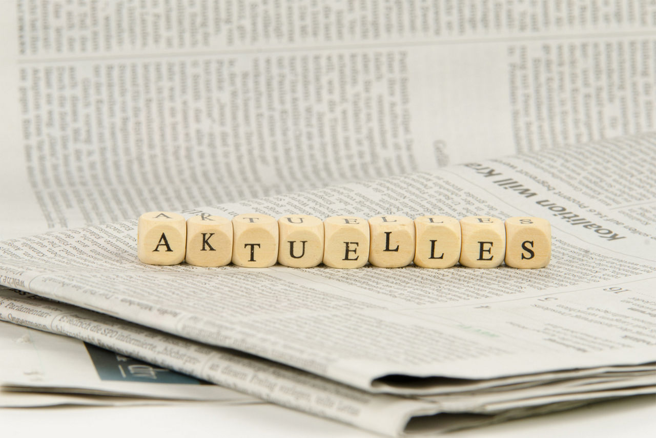 Würfel mit Buchstaben liegen auf einer Zeitung und sind als das Wort "aktuelles" angeordnet