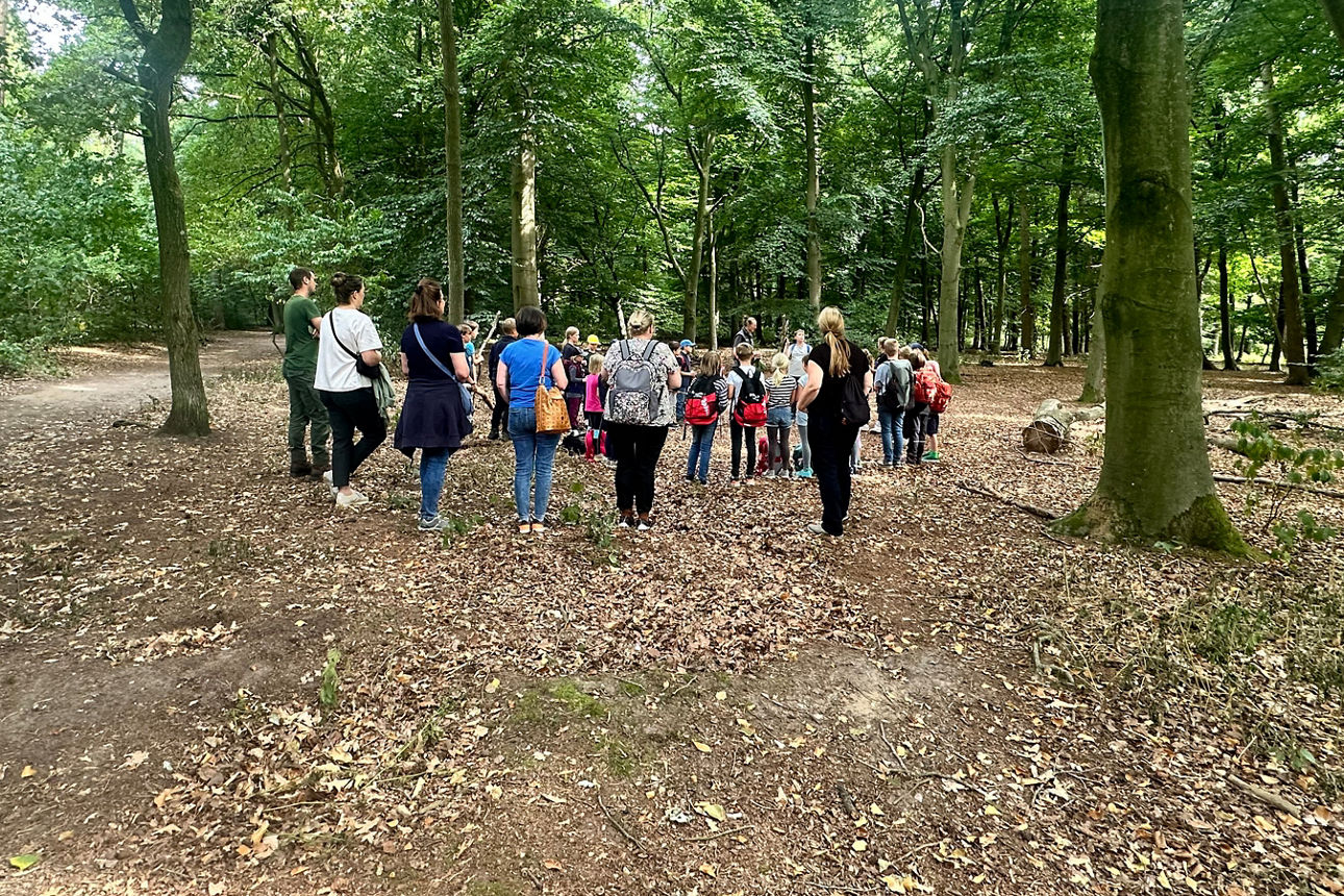 Eine Gruppe aus Kindern und Erwachsenen steht in einem Kreis im Wald.