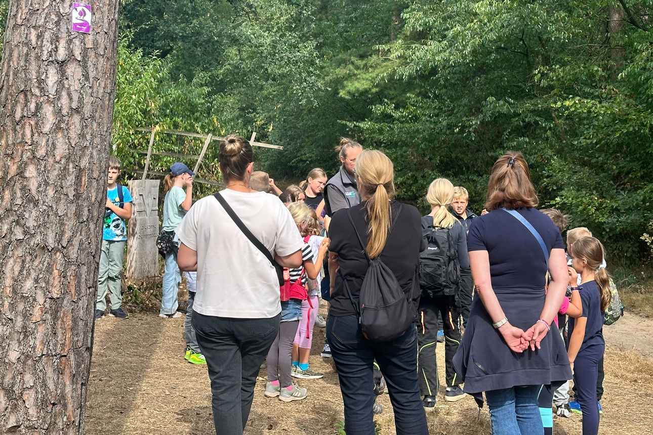 Eine Gruppe Kinder und Erwachsene versammelt sich neben einem Baum.