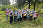 Eine Gruppe von Kindern steht im Volksbankwald und hält sich Fahnen vors Gesicht