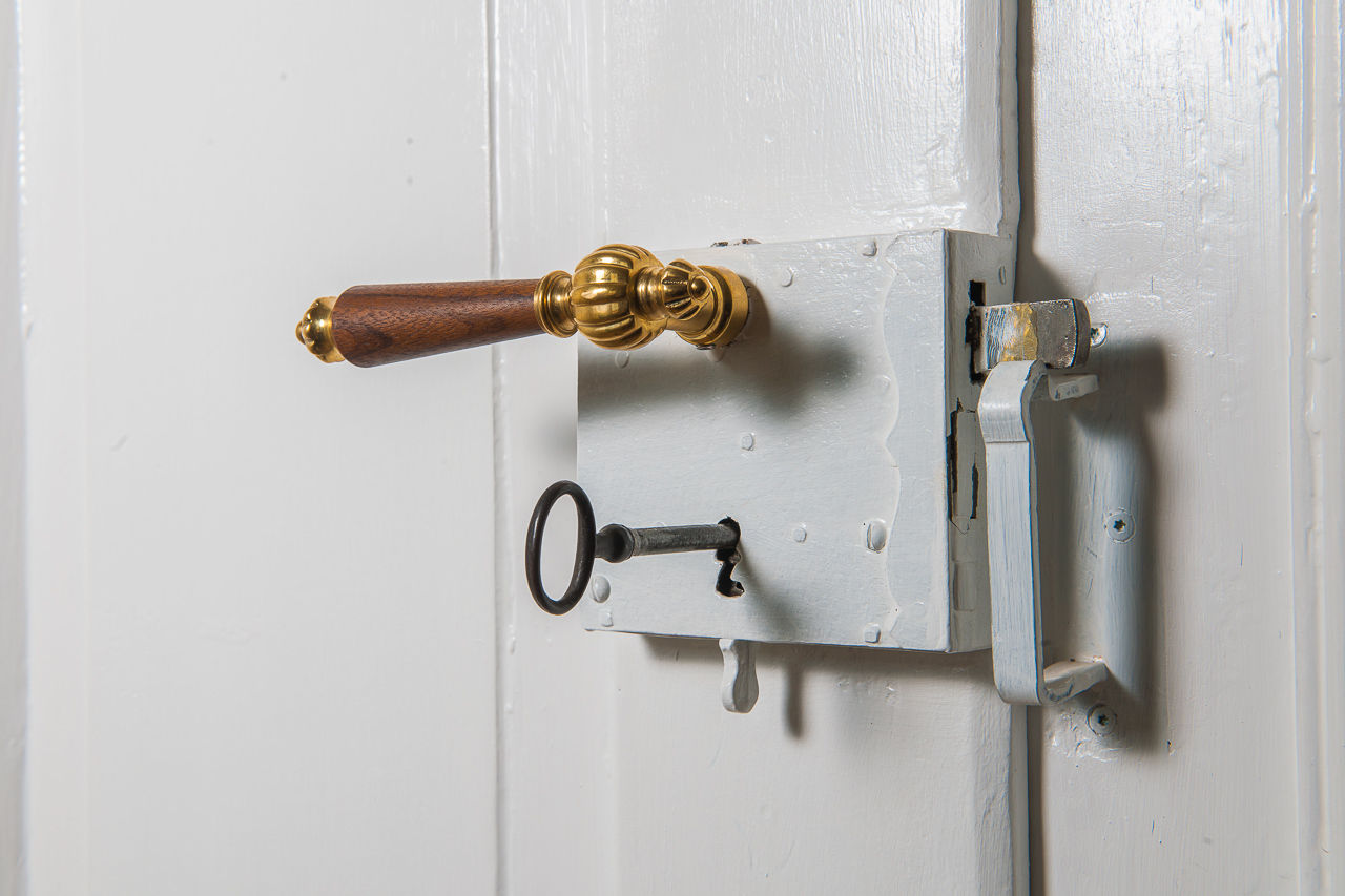 Ein goldener Türgriff an einer weißen Tür und ein silberner Schlüssel steckt im Schloss