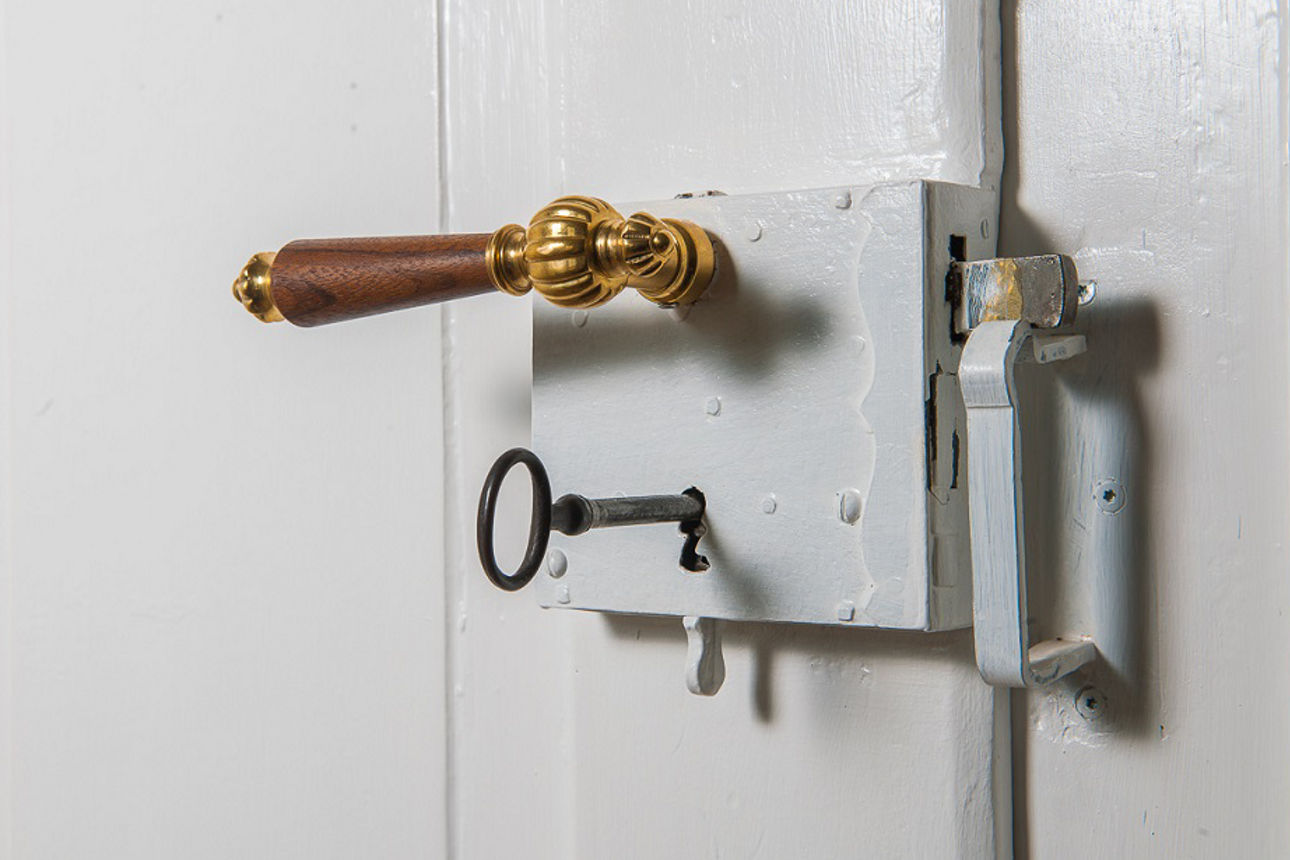 Ein goldener Türgriff an einer weißen Tür und ein silberner Schlüssel steckt im Schloss