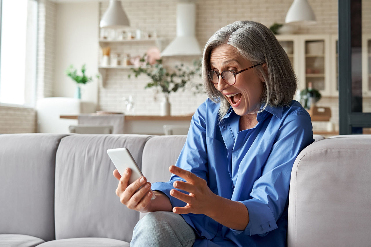 Eine Frau sitzt auf der Couch und bedient begeistert ihr Handy.