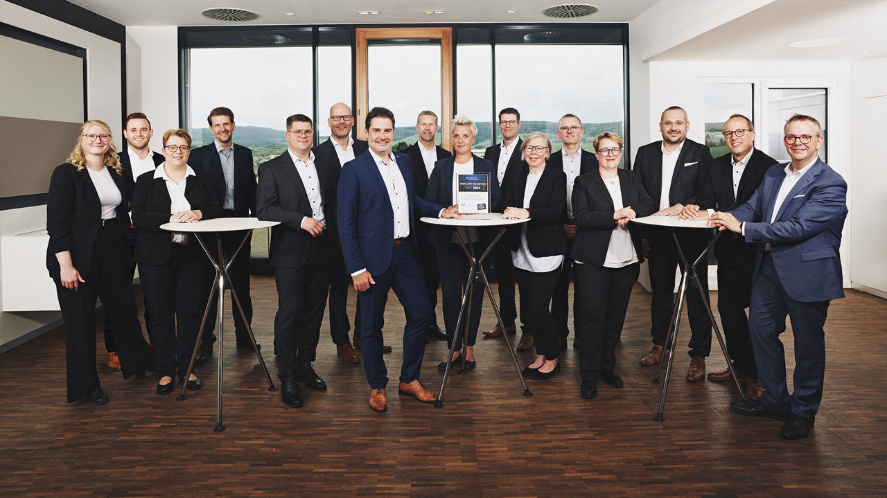 Die Mitarbeitenden der Abteilung Private Banking stehen in einer Gruppe um ein paar Stehtische herum