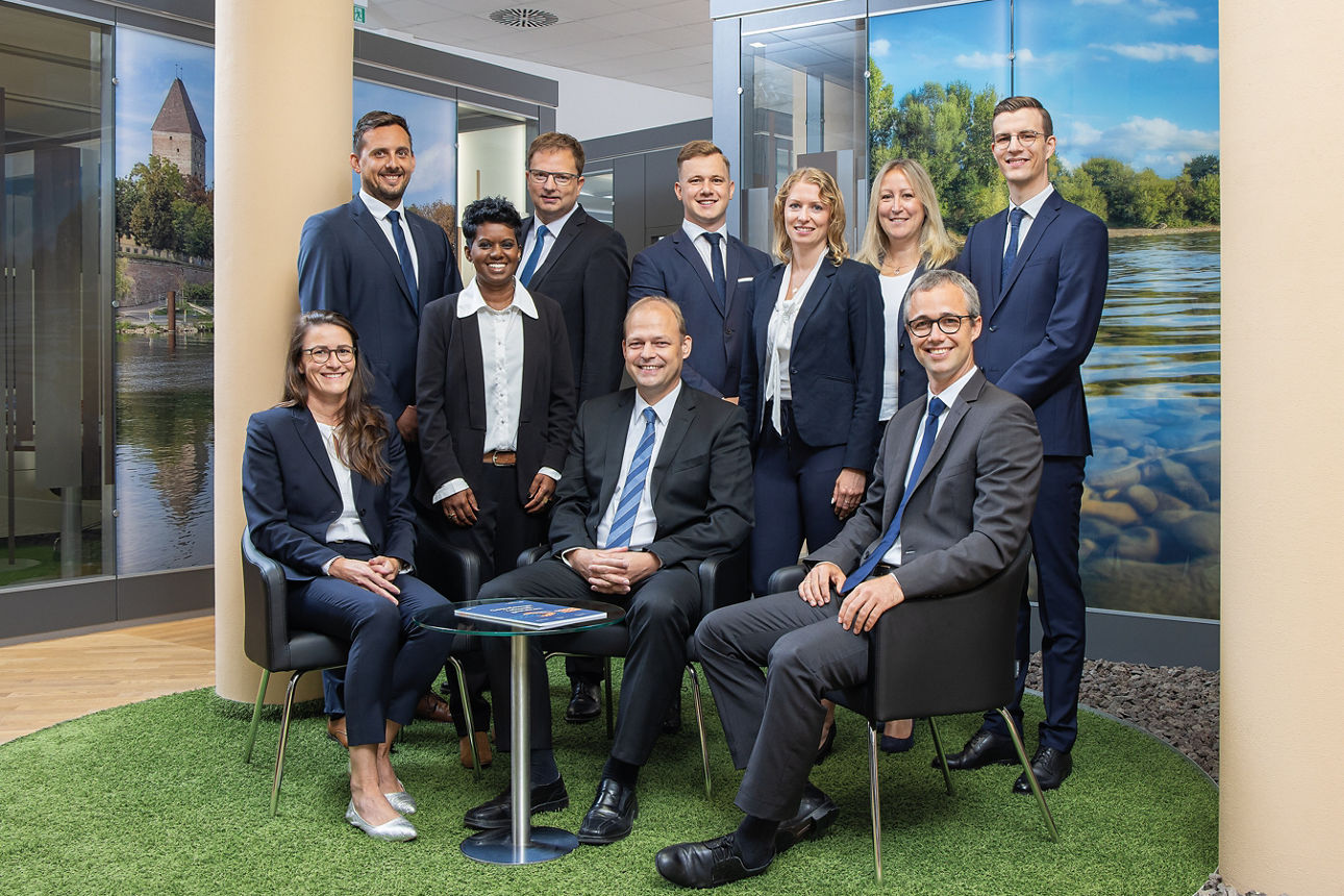 4 Frauen und 6 Männer sitzen und stehen um einen kleinen runden Tisch