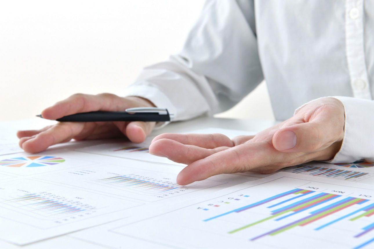 Hände von einem Mann mit einem Stift und Dokumenten auf dem Tisch. 