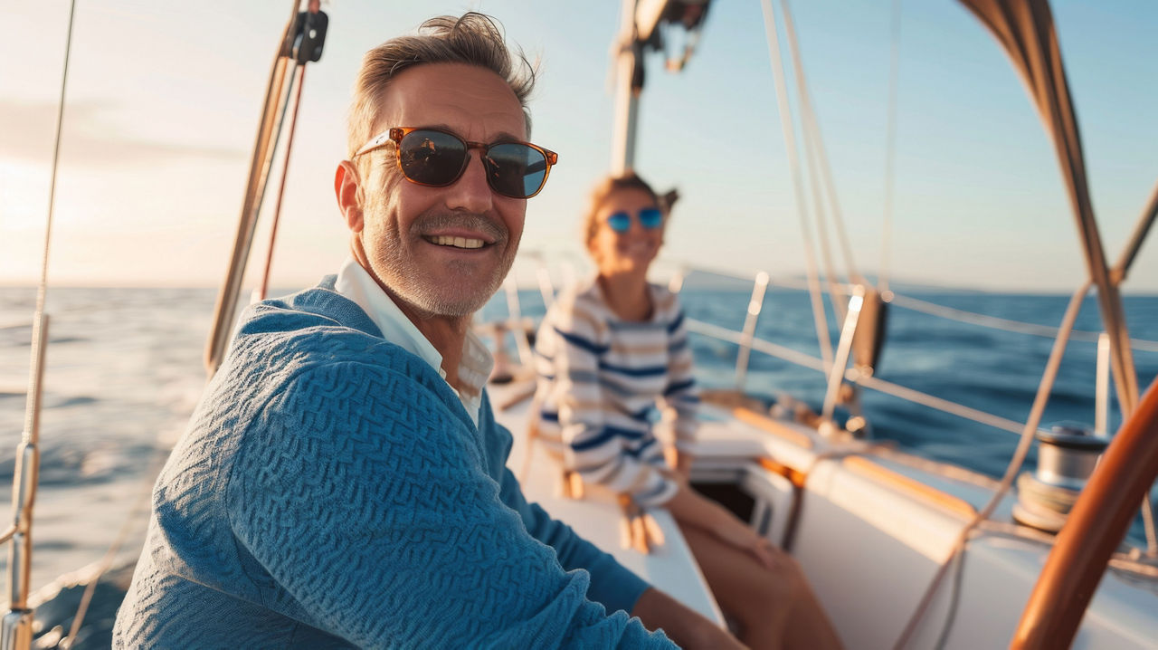 Ein lächelndes Paar in legerer Kleidung und Sonnenbrille genießt einen entspannten Tag auf einer Yacht mit einem klaren blaue