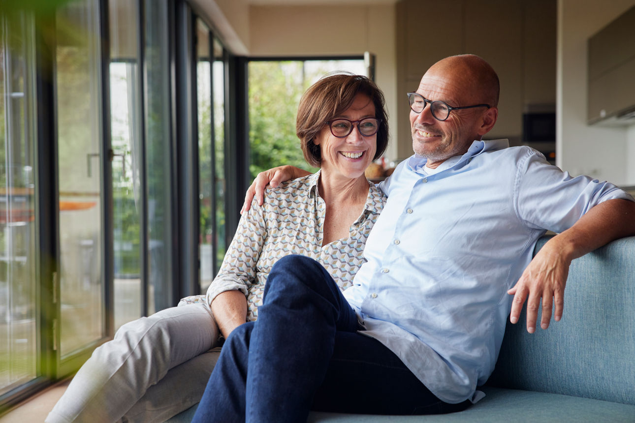 Cheerful senior woman with man sitting on sofa together at home