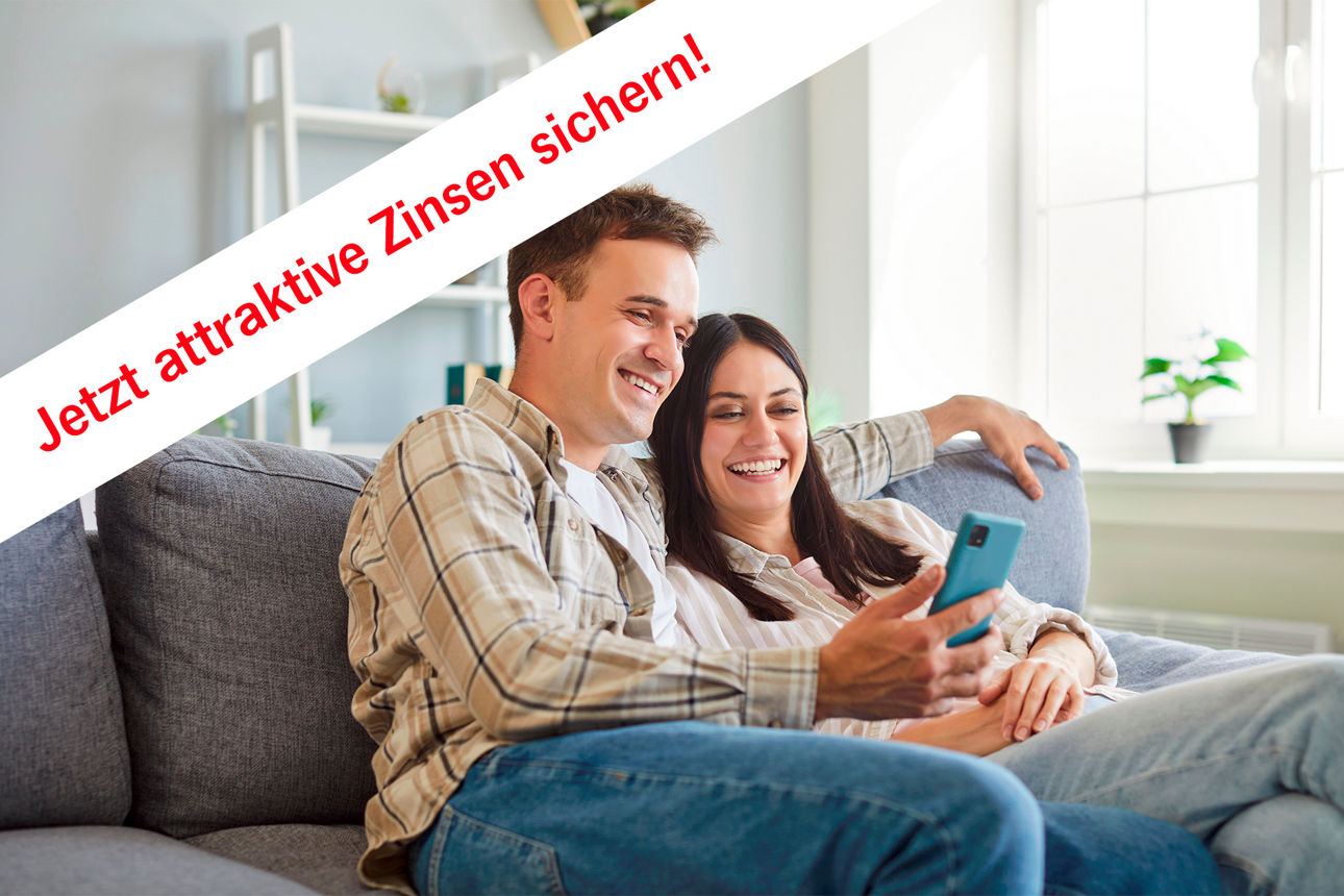 Ein junges Paar sitzt auf dem Sofa und liest zusammen in einem Handy