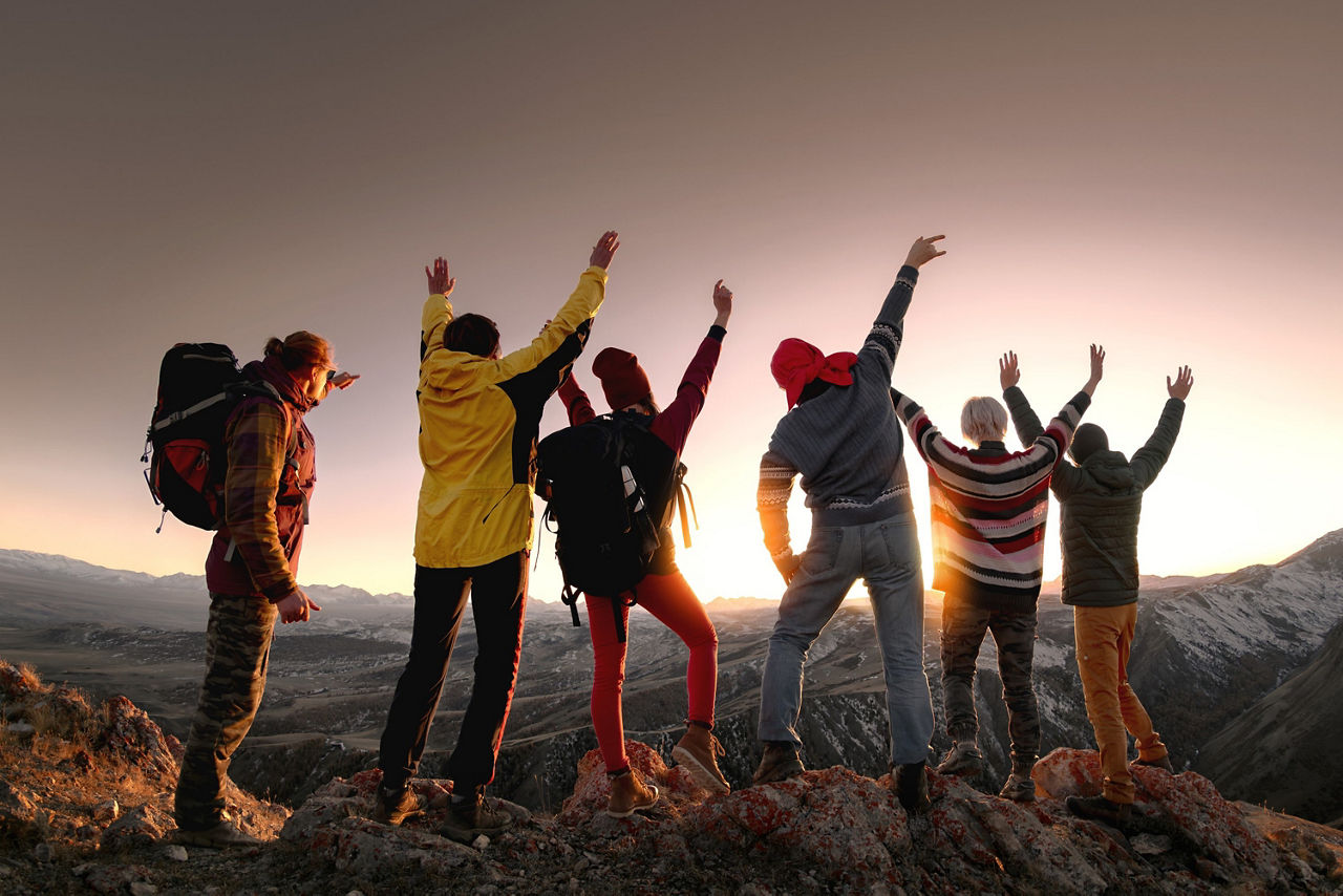 Eine Gruppe junger Leute steht im Sonnenuntergang auf einem Berg