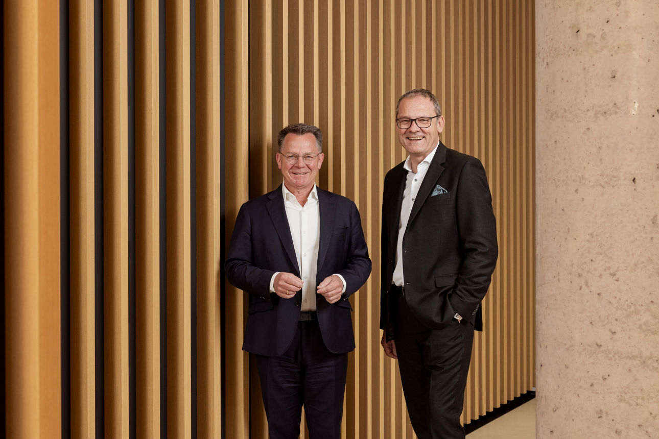 Unser Vorstandsmitglied Hr. Spietenborg steht neben unserem Privatkunden Bereichsleiter Hr. Vogelbacher vor Holzlamellen