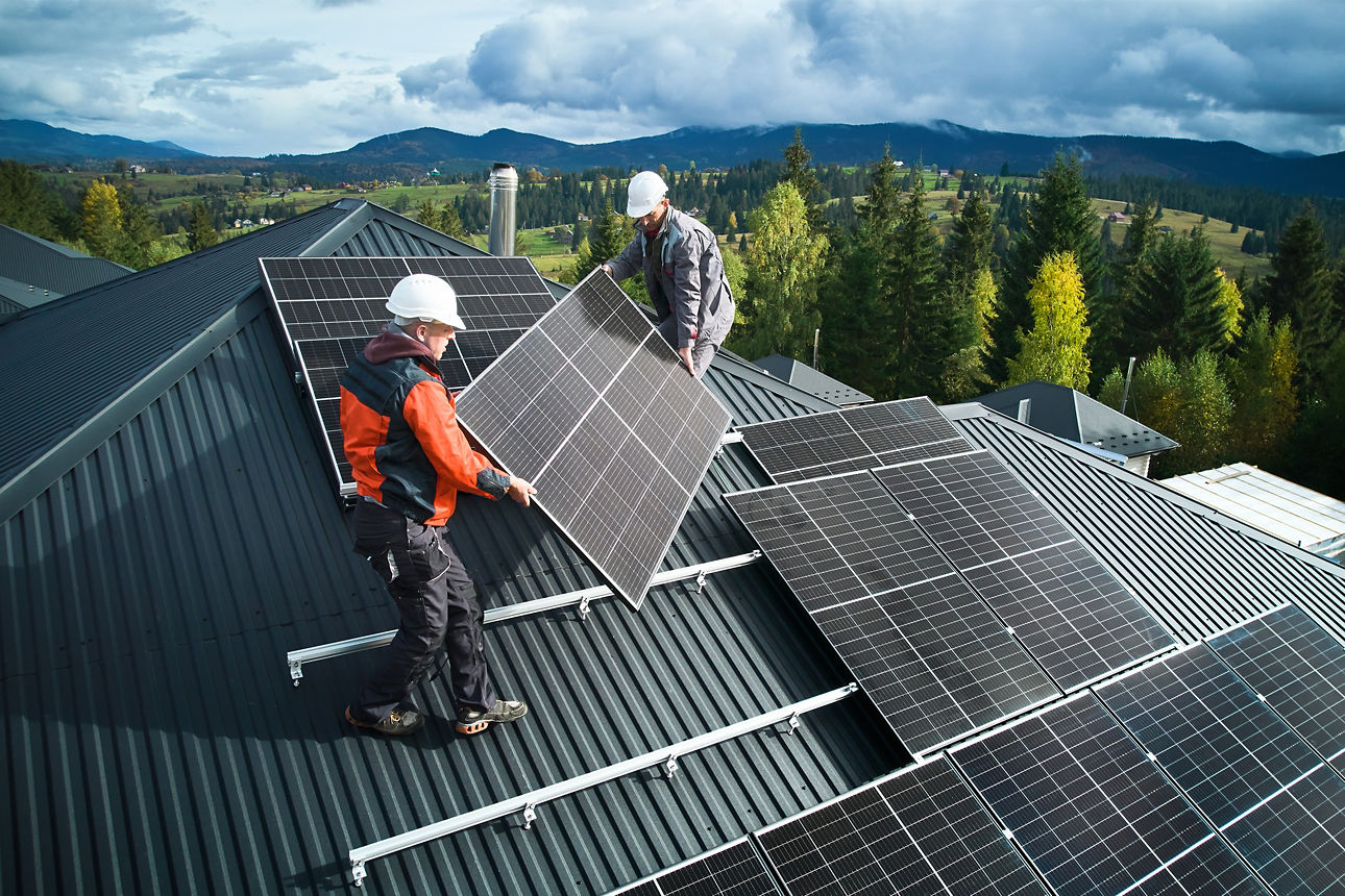 Zwei Arbeiter legen Solarpanele auf ein Dach