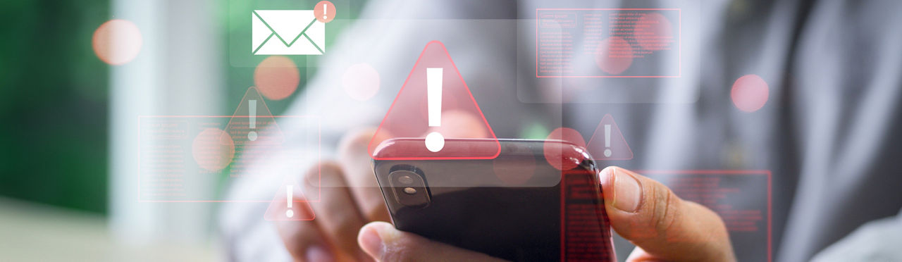Person tippt auf Handy ein, Warnzeichen werden angezeigt