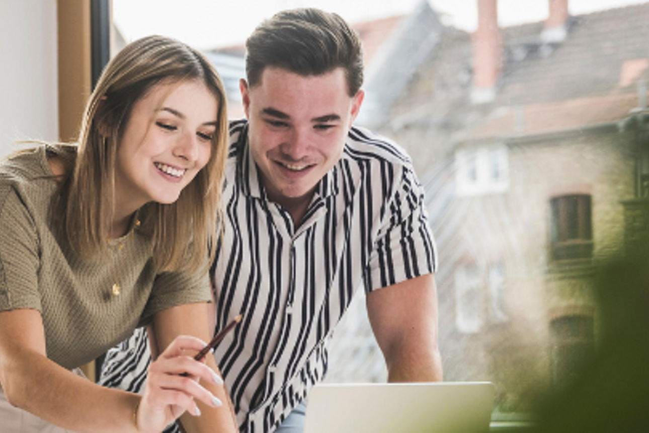 Mann und Frau schauen gemeinsam lächelnd auf einen Laptop