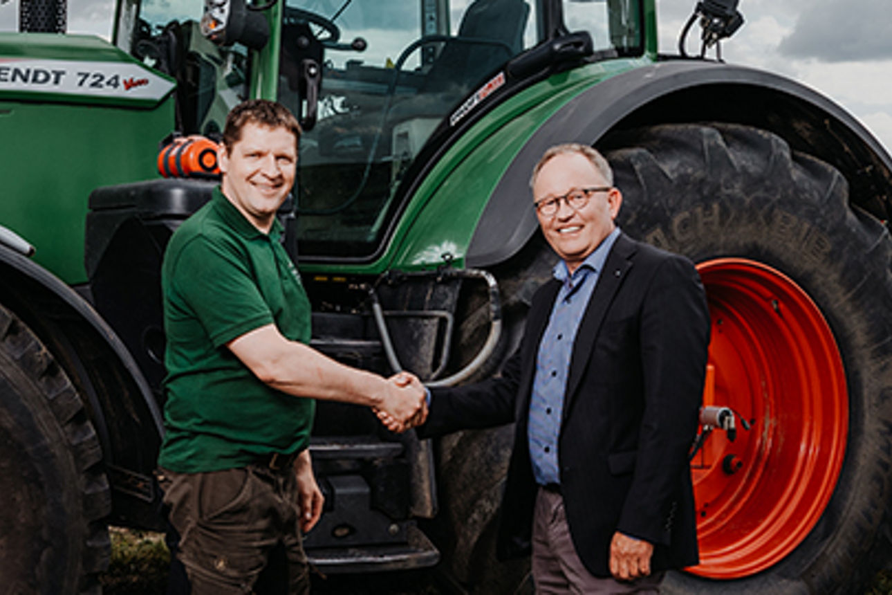 2 Männer schütteln sich vor einem Traktor die Hände