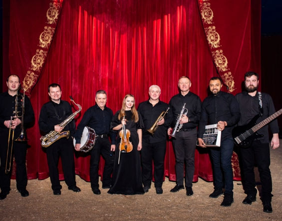 8-köpfiges Orchester-Team vor dem roten Zirkusvorhang